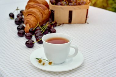 Beyaz arka planda taze kruvasan ve kirazlı siyah çay. Bahar kahvaltısı kavramsal kompozisyonu
