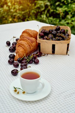 Beyaz arka planda taze kruvasan ve kirazlı siyah çay. Bahar kahvaltısı kavramsal kompozisyonu