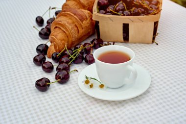 Beyaz arka planda taze kruvasan ve kirazlı siyah çay. Bahar kahvaltısı kavramsal kompozisyonu