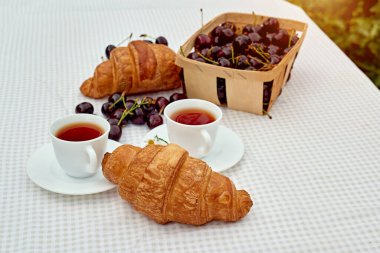 Beyaz arka planda taze kruvasan ve kirazlı siyah çay. Bahar kahvaltısı kavramsal kompozisyonu