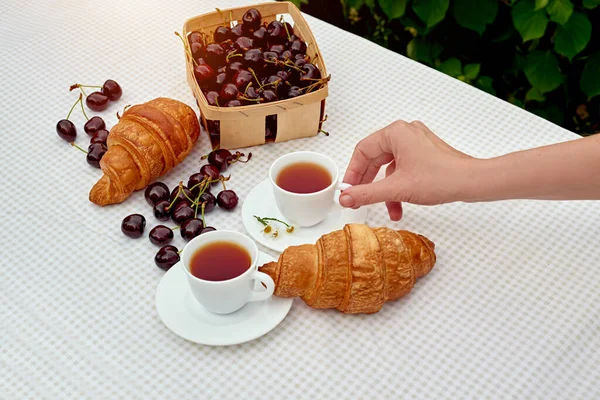 Beyaz arka planda taze kruvasan ve kirazlı siyah çay. Bahar kahvaltısı kavramsal kompozisyonu