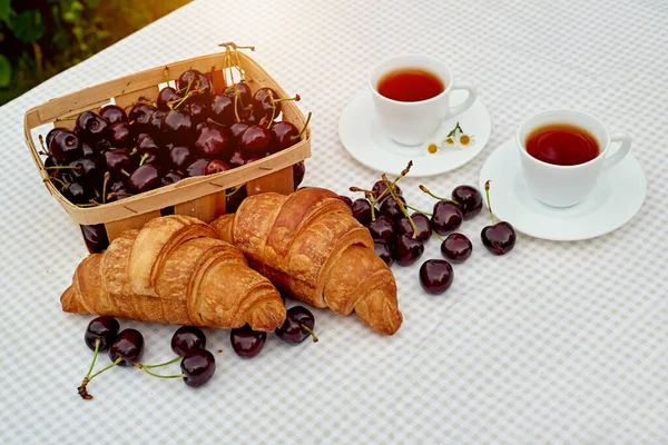 Beyaz arka planda taze kruvasan ve kirazlı siyah çay. Bahar kahvaltısı kavramsal kompozisyonu