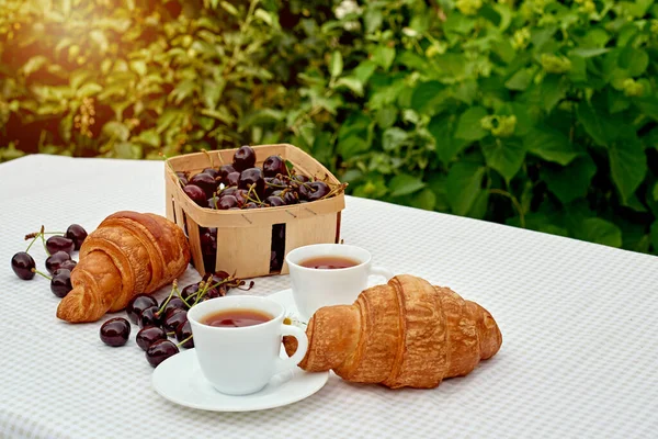 Beyaz arka planda taze kruvasan ve kirazlı siyah çay. Bahar kahvaltısı kavramsal kompozisyonu