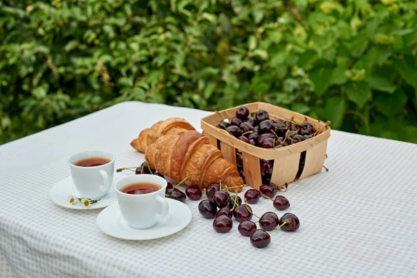 Beyaz arka planda taze kruvasan ve kirazlı siyah çay. Bahar kahvaltısı kavramsal kompozisyonu