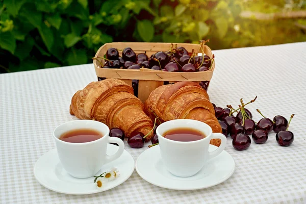 Beyaz arka planda taze kruvasan ve kirazlı siyah çay. Bahar kahvaltısı kavramsal kompozisyonu