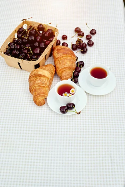 Beyaz arka planda taze kruvasan ve kirazlı siyah çay. Bahar kahvaltısı kavramsal kompozisyonu