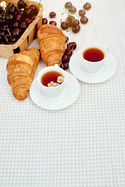 Beyaz arka planda taze kruvasan ve kirazlı siyah çay. Bahar kahvaltısı kavramsal kompozisyonu