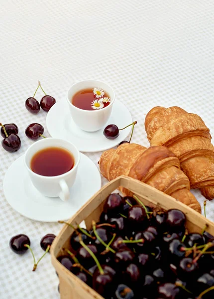 Beyaz arka planda taze kruvasan ve kirazlı siyah çay. Bahar kahvaltısı kavramsal kompozisyonu