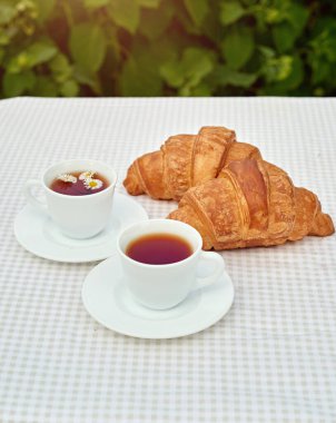 Masada beyaz arka planda papatya çayı ve taze kruvasan olsun. Bahar kahvaltısı kavramsal kompozisyonu