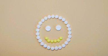 Bej arka planda sarı beyaz haplardan gelen gülen yüz. Sağlıklı ve keyifli.