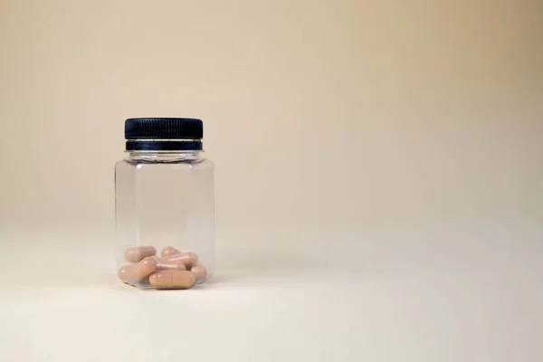 Bej arka planda plastik bir şişedeki kapsüller. Kadınlar için haplar ve sağlıklı yaşam