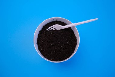 Tencerede siyah toprak ve mavi arka planda beyaz çatal. Çiçek dikmek için. 