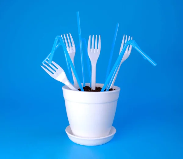 Mavi arka planda beyaz bir tencerede çatallar ve pipetler. Topraktaki plastik..