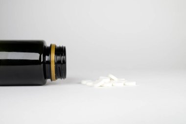 Beyaz arka planda beyaz haplı siyah şişe. Uyuşturucu ve insan bağımlılığı. Kötü ilaçlar ve kötü kimyasallar..