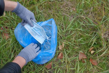 Tıbbi maske mavi bir çöp torbasında. Gönüllü olarak. Ormanda çöp toplama