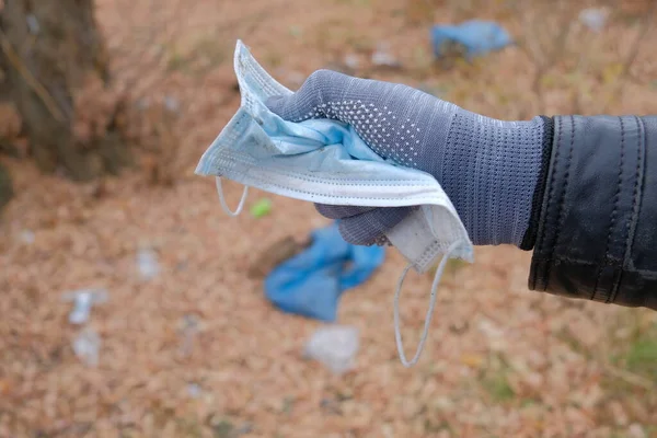 Eller ormanın arka planında bir maske tutuyor. Bir gönüllü ormanda çöp topluyor. Dünya Günü.
