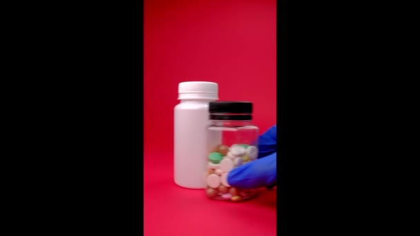 Weißes Gefäß Und Transparentes Gefäß Mit Farbigen Pillen Auf Rotem — Stockvideo