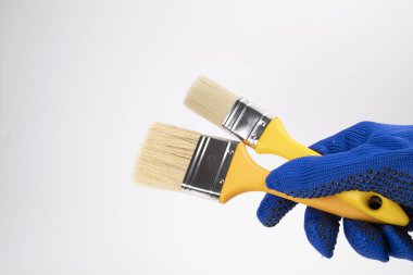 Beyaz arka planda el ele iki fırça. Eldivenin içinde fırça tutan bir el