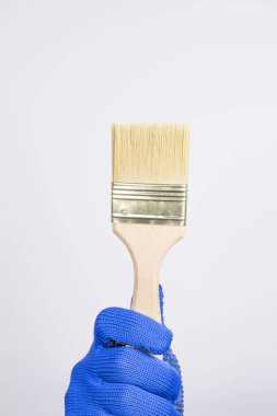 Beyaz arka planda temiz boya fırçası. Mavi eldivenli bir el büyük bir boya fırçası tutar. Yapı ve boya fırçası