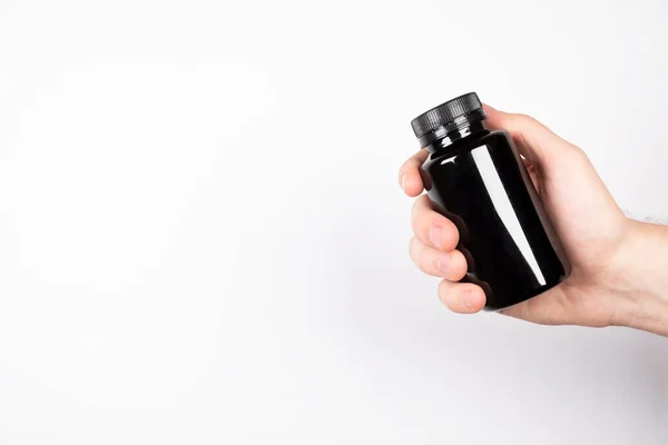Beyaz arka planda siyah şişe. Bir adamın elinde bir kutu hap var. Vitaminli ve mineralli kavanoz. Patent tabletleri