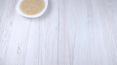 Masanın üzerinde beyaz bir tabakta pirinç. El masaya bir tabak pirinç koyar.