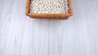 Kadın elleri masaya bir kase beyaz fasulye koydu. Masada beyaz fasulye var.