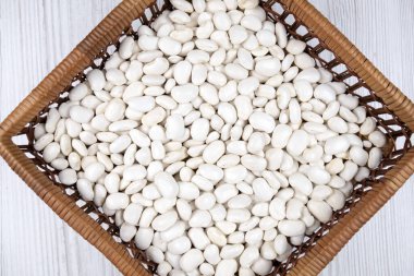 Masadaki hasır kasede beyaz fasulye taneleri.