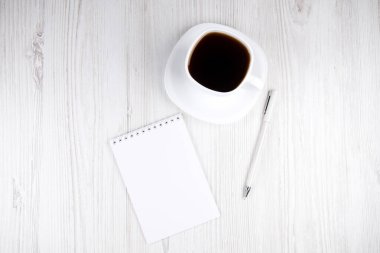 Beyaz bir fincan kahve, not defteri ve tahta bir masanın üzerindeki beyaz kalem.