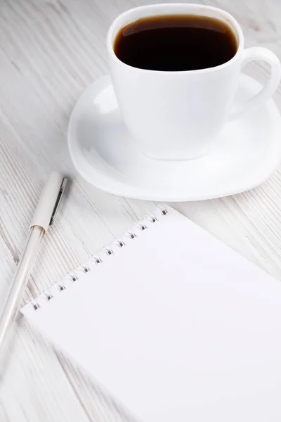 Bir fincan kahve, bir defter ve tahta bir masanın üzerinde beyaz bir kalem. Ofis işi