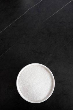 Siyah arka planda bir kasede beyaz şeker granülleri, boş alan