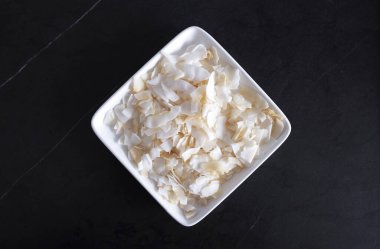 Siyah arka planda beyaz kare bir tabakta hindistan cevizi taneleri. Tabak taş masanın üzerinde.