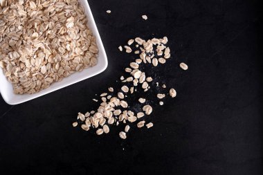 Beyaz tabakta yulaf ezmesi, siyah masada uçan yulaf ezmesi, boş yer.