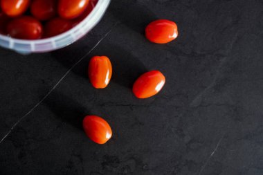 Kovada küçük domatesler ve siyah bir masada üç domates.