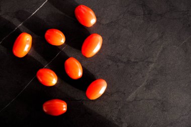 Güneş tarafından aydınlatılan siyah arkaplandaki küçük domatesler