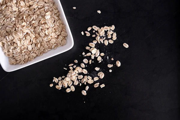 Beyaz tabakta yulaf ezmesi, siyah masada uçan yulaf ezmesi, boş yer.