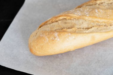 Siyah bir masada beyaz ekmek parşömen üzerinde. Taze pişmiş ekmek, yakın plan.