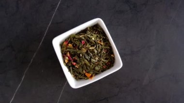 Katkı maddeleri içeren yeşil çay yaprakları siyah bir masada beyaz bir tabakta görünür. Yeşil çay tercihi