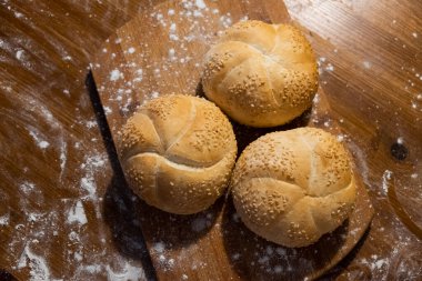 small buns with sesame seeds on a board sprinkled with flour top view. Fresh bakery. Food breakfast. Sandwich buns