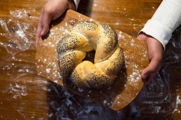 man holds a bun with poppy seeds on the board. Flour on the table. Bakery products