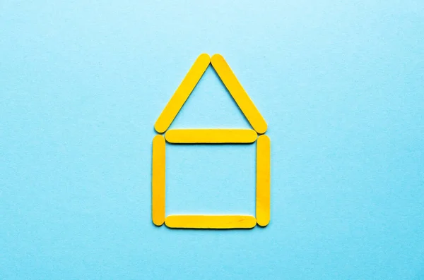 House made of wooden yellow sticks on a blue background. Construction of houses.