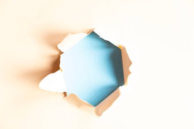 hole in beige paper on blue background, space for text