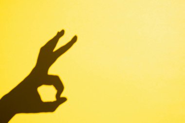 shadow gesture ok on yellow background, free space.