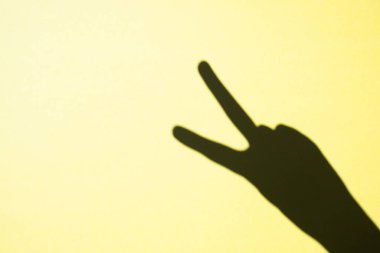 shadow gesture victory on yellow background, free space
