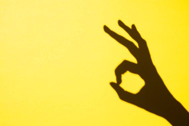 shadow gesture ok on yellow background, free space.