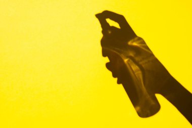 shadow hand holding a spray bottle on a yellow background, free space. Cosmetics for face and body