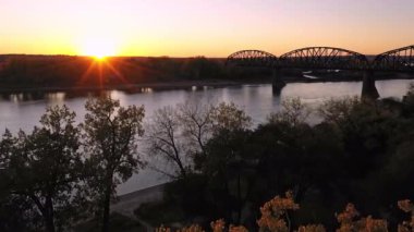 Güneşin batışına doğru Missouri Nehri boyunca uzanan tarihi demiryolu köprüsü ile birlikte uçuyor..