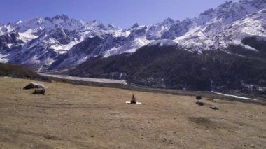 Nepal 'deki Kyaniji Vadisi' nde yoga yapan bir adam arka plandaki karlı dağlara bakarak etrafında uçuyor..