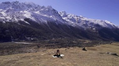 Nepal 'deki Kyaniji Vadisi' nde yoga yapan bir adam arka plandaki karlı dağlara bakarak etrafında uçuyor..