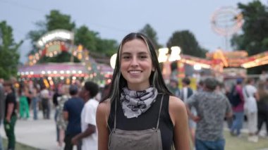 İnsanlar arka planda yürürken karnavalda ayakta durup gülümseyen genç bir kadına yaklaş..