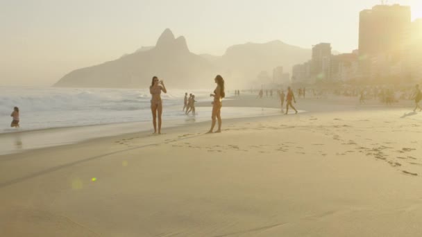 リオデジャネイロ ブラジル 2013年6月 スローモーション ドイス イルマオスと夕暮れ時の街並みを背景にイパネマビーチでビキニを着た2人の若い女性のトラッキングショット — ストック動画